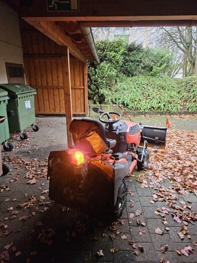 Einsatz-Fahrzeug hinten Rasentraktor mit Rücklicht in einer Garage, umgeben von Mülltonnen und Laub.